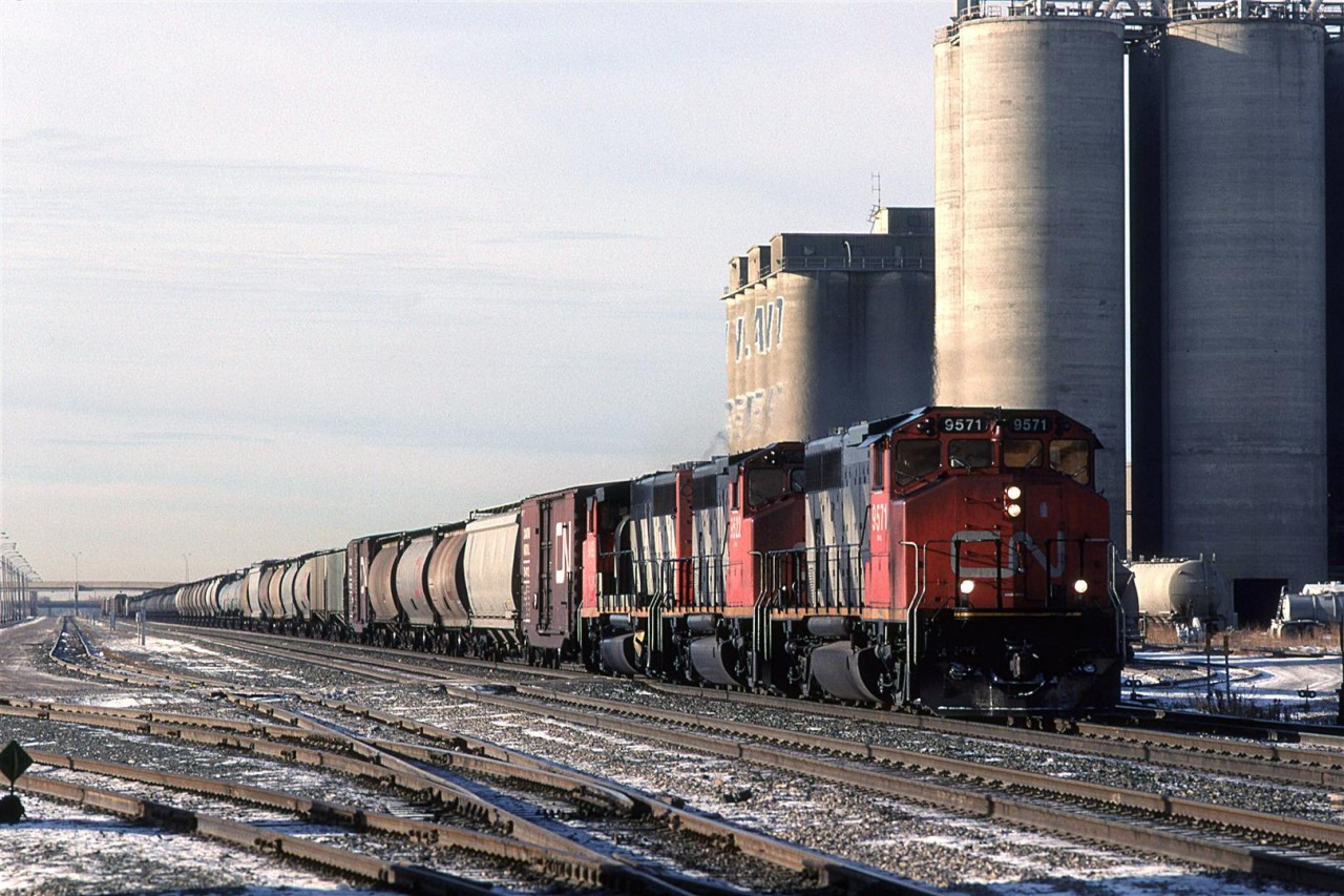 It may not be immediately obvious, but this is train 218. Look carefully and you will see tank cars aqnd auto racks way in the distance.
Bissell Yard seems to be rather empty this day. Inland Cement's huge silos dominate the background. Just to the right, out of frame, is where the Sangudo sub splits off.
That looks to be an interesting hopper/tank car immediately right of the lead locomotive.