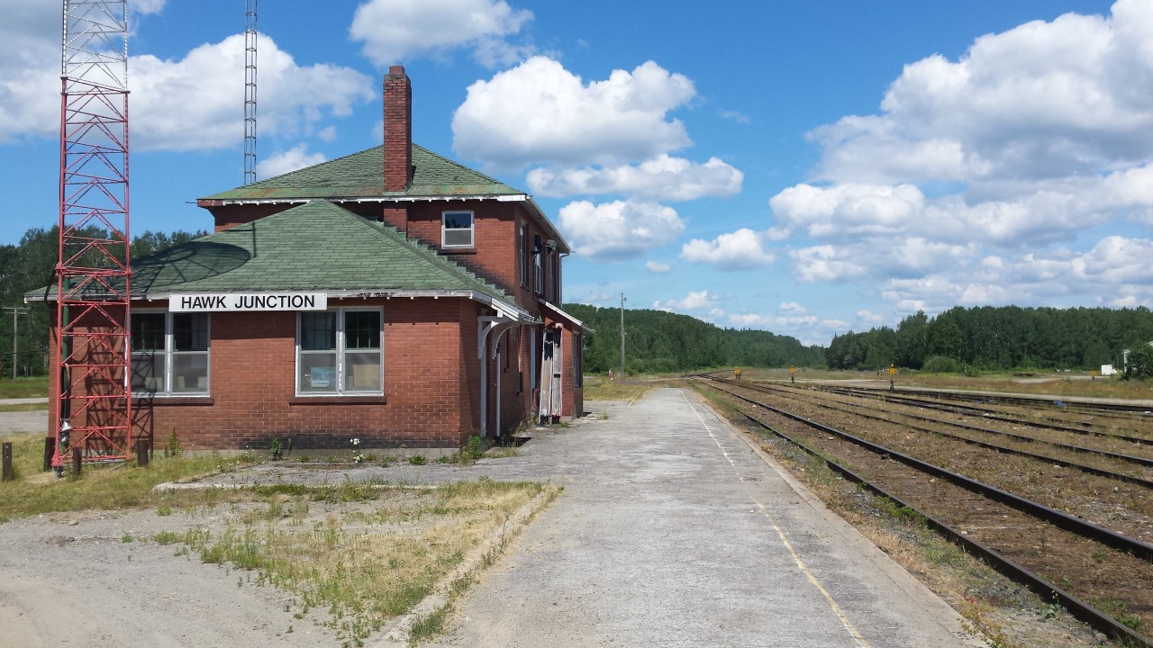Let's go for a long weekend camp at Agawa Bay. Such was the plan. Go north, dip my feet in Superior once again, and forget southern Ontario even exists. All while basking in the gorgeous weekend weather we were provided. I needed a new pair of shoes to go hiking with the kids, and, since Wawa sported not only a Tim Hortons, but a shoe store as well, the van was loaded, and further north we went. Upton arrival, I noted the sign for Hawk Junction, checked maps, and discovered that it's just up the road. Going there? You betcha! 

Presented is the station as of July 30, 2016. Still standing, watching over a yard that sees use, but nothing that resembles the early days. Recanting facts provided by Mr. Mooney himself, how the line into the hills was the old line to the docks at Michipicoten, which saw use by the Wisconsin Central hauling products from the long gone sinter plant to waiting boats in the harbour. 

We heard a southbound hollering for something around midnight the previous night, presumably a moose or bear on the tracks. The only indication of trains passing through. 

PS. Last one to leave the Hawk turns out the lights. ;)