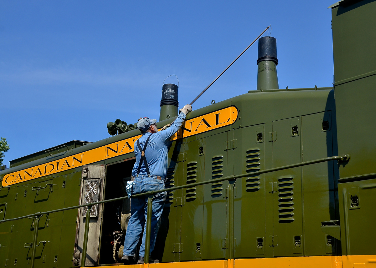 Capping the stacks. A volunteer at Exporail is capping the second of two stacks on CN 1382 after shutting down the engine and then pulling two buckets out of the long hood. The engine has just performed some switching moves.
