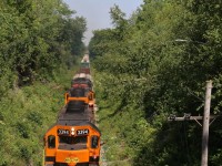 Exhaust and plus 30 degree heat distorts the background scenery as GEXR train 431's power with a combined 9600 hp barely seems enough as the train and its well worn trio of SD's slowly claw their way up the Niagara Escarpment at Limehouse, complimented by a friendly wave from a crew member. The train has just been cleared to Acton as a brush cutting crew has just cleared the tracks ahead. 