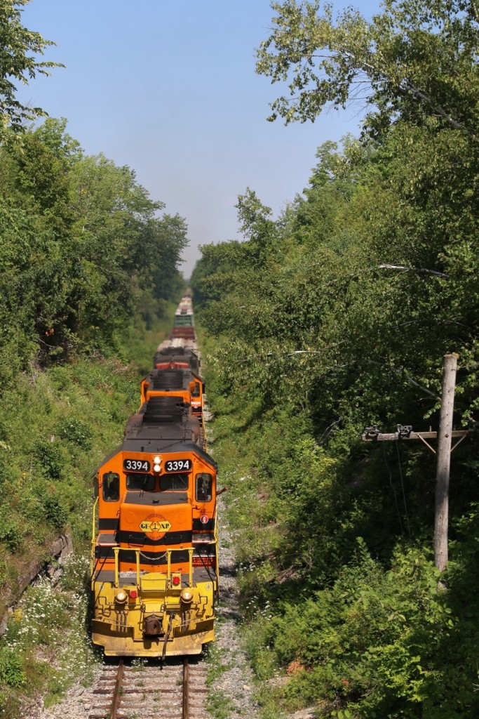 Exhaust and plus 30 degree heat distorts the background scenery as GEXR train 431's power with a combined 9600 hp barely seems enough as the train and its well worn trio of SD's slowly claw their way up the Niagara Escarpment at Limehouse, complimented by a friendly wave from a crew member. The train has just been cleared to Acton as a brush cutting crew has just cleared the tracks ahead.