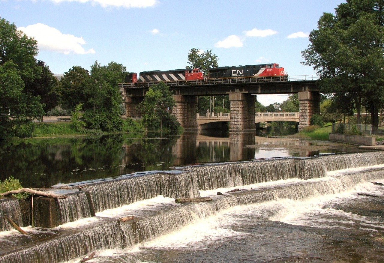 CN 2244 and CN 5540 striped with additional power parade CN 710 high atop the iconic bridge structure over the Napanee River adding grandeur to the picturesque Springside Park and peaceful waterfall.  In order to capture this angle to catch a eastbound and to include the whole of the waterfall, I camped (with permission) under shade on adjoining property owned by Gibbard Furniture, Canada's oldest furniture factory (at the time at least).  Employees gained a new perspective that day respecting patience, nearby beauty and railfanning.