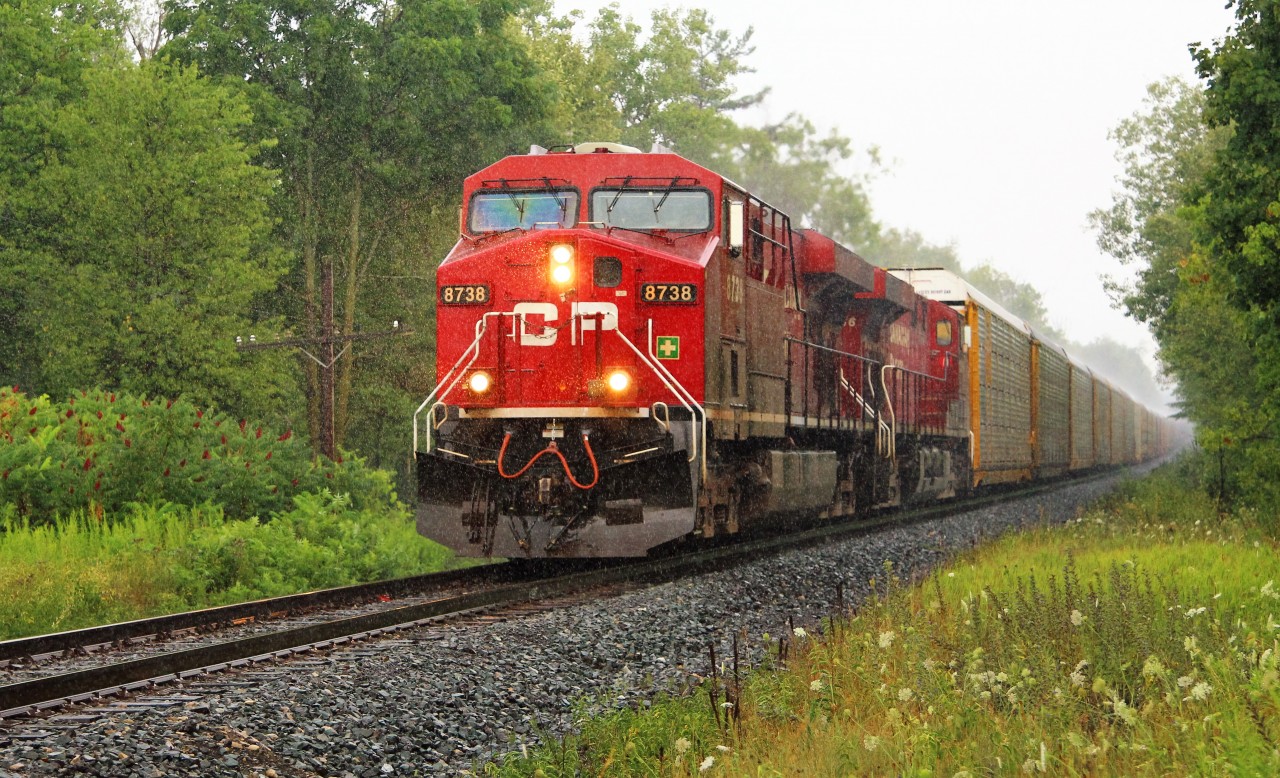 After a day of seeing nothing for trains, it started to pour rain so I went to turn off the scanner and low and behold, a clearance from Guelph Junction for a westbound train. Maybe it would stop raining before it got there (not that I wanted it to because we really need it). Not in your life. So, out of the front seat of my truck and through the passenger window, we find CP 8738 leading CP 8866 through the rain past MM43 with 9435 feet of auto racks and brand new tanker cars.