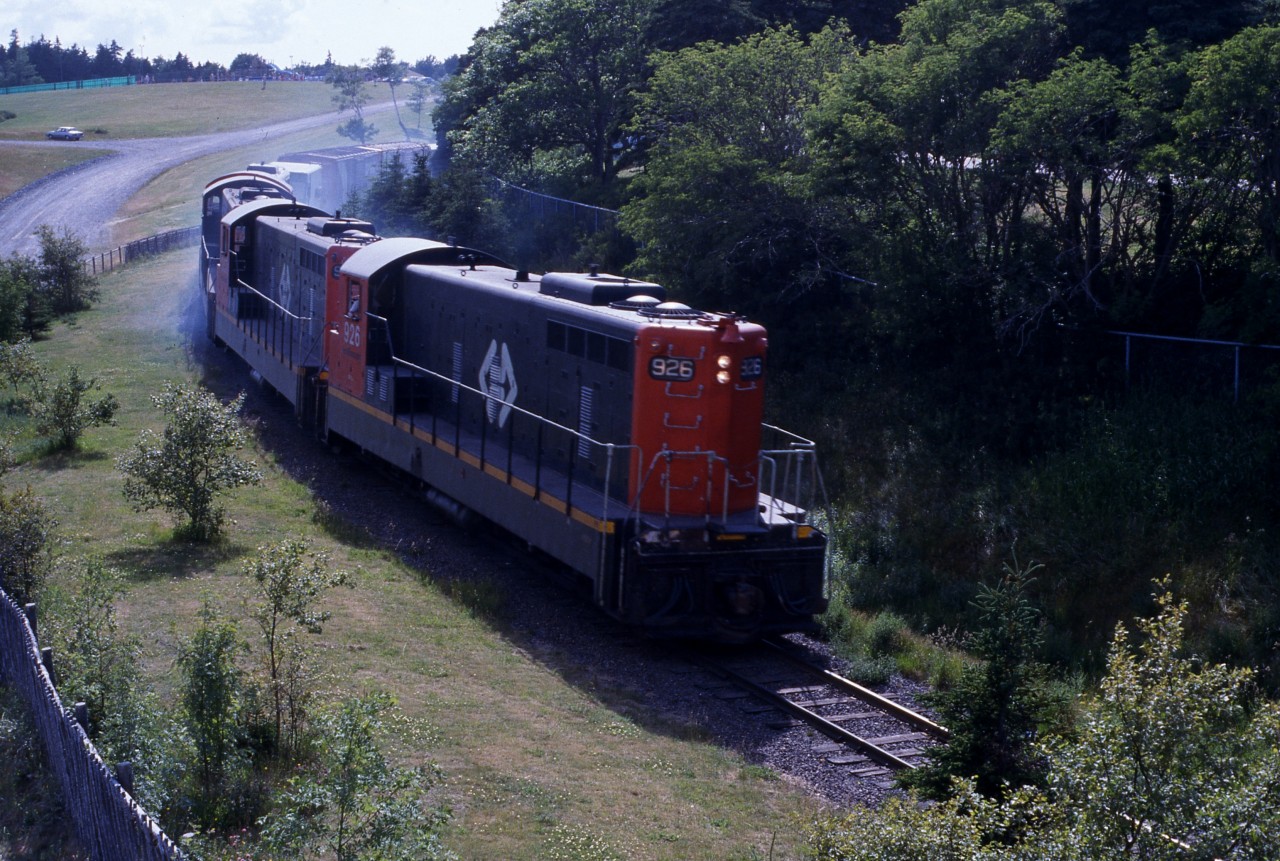 DOWNGRADE AT BOWRING PARK - Brake shoe smoke envelopes the head end power of Terra Transport Extra 926 East on the hot and humid Sunday afternoon of July 19, 1987. With only a few miles left to go on it's 547 mile  trans island journey, lead engine NF210 #926 and three sisters haul two CP rail boxcars and about twenty green inter-modal containers to it's final destination, the railyard in the capital city of St. John's. While travelling the 138 miles from Corner Brook to Bishops's Falls, a coach was added, thus making the former train known as #204, for that portion, Mixed Extra 926 East on the narrow gauge line.