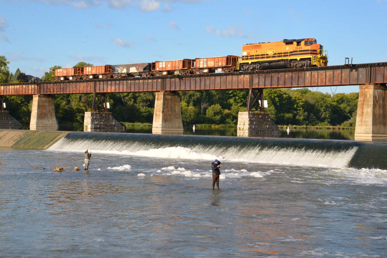 RLHH 3049 slowly trundles north across the iconic bridgework over the Grand River at Caledonia, with its 1st trip of the day, hauling  five aged / renumbered ballast cars (NERX 134, 122 123, 136 and OWSX 250730) just as the sun sneaks a timely peak out from behind a few cloud formations. The entire main from Nanticoke to Simpson Junction is in the midst of receiving new ballast.  These 5 ballast cars were delivered to Hagersville by truck (OWS Railroad Construction & Maintenance, Petrolia) and deposited directly onto the rails of siding HD34.  Likewise ballast originating from Woodstock and even home town Rock City is trucked in and stock-piled adjacent to HD34. Each ballast train is trans loaded within 45 minutes, while snoozing on HD34, by RF Almas Co. Ltd (Hagersville) using a rugged CAT 1T286 Payloader.