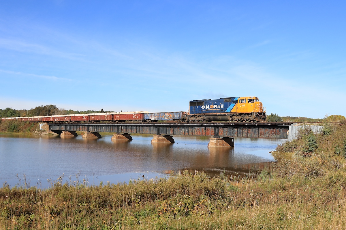 ONT 308 crosses the Frederick House River with 2104 leading 27 cars.  The covered gondolas are full of copper and zinc concentrate from the Kidd Mine.