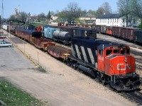 CN GP40-2L(W) 9646 handles the London Auxiliary past Woodstock station and yard, going to a wreck near Paris. Passenger trains were being wyed at Woodstock to return to London due to the mishap, and passengers are visible on the platform awaiting their train. The array of equipment behind the 9646 are a pair of flatcars loaded with rails and ties, a pair of old repurposed baggage cars, flatcars loaded with spare wheelsets and trucks, a wrecking crane, bunk cars and a caboose.
<br><br>
Visible in the yard are a variety of American road cars including C&NW, Rock Island, N&W, Missouri Pacific, Chessie System, Southern, and GTW. A CN switcher and transfer caboose are also mixed in amid the cars.