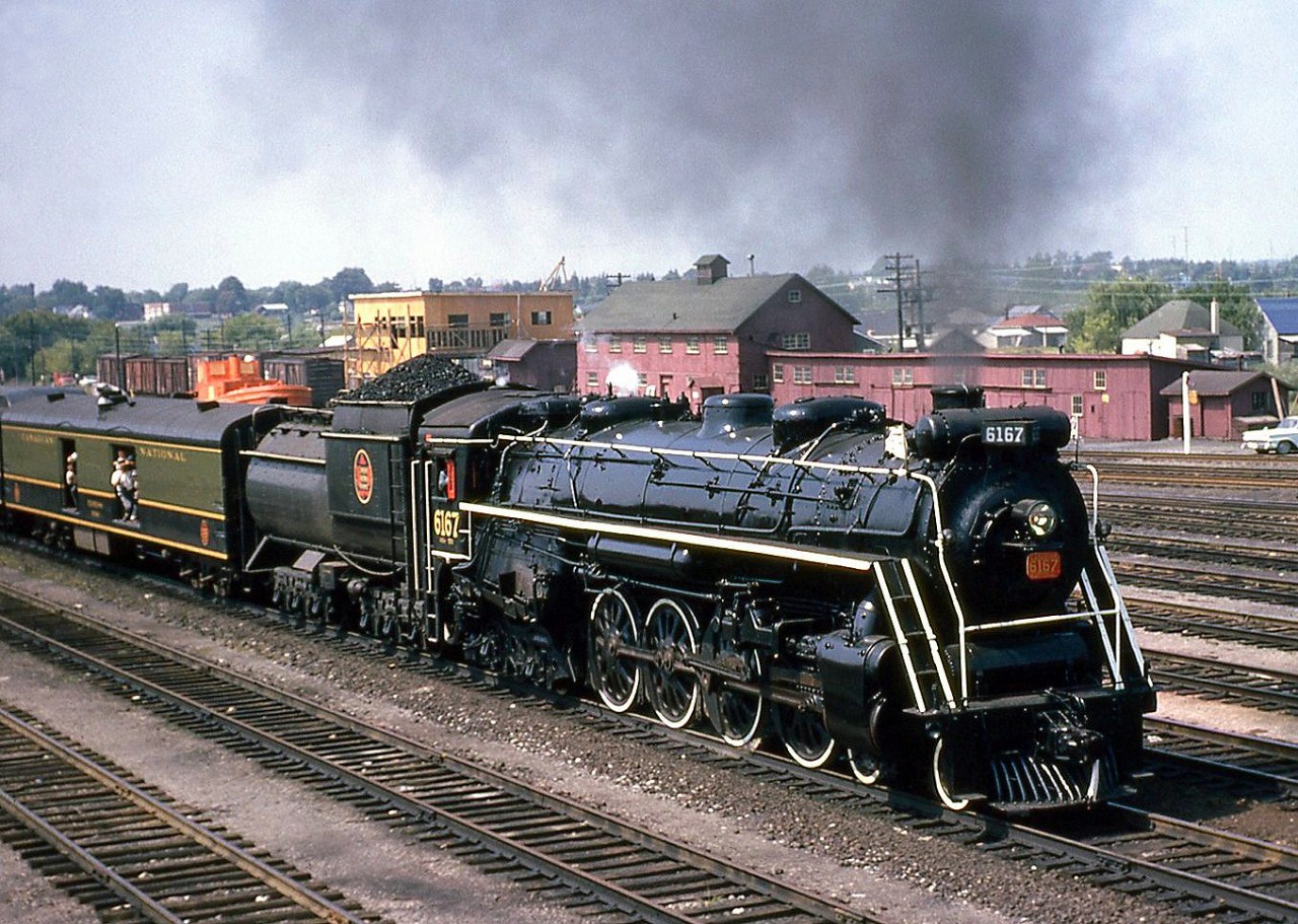CNR U2e Northern 6167 operates on a UCRS fantrip from Toronto to Picton, shown in Belleville yard on August 26th, 1962 with excursion goers leaning out of the open doorways of the baggage car immediately behind.