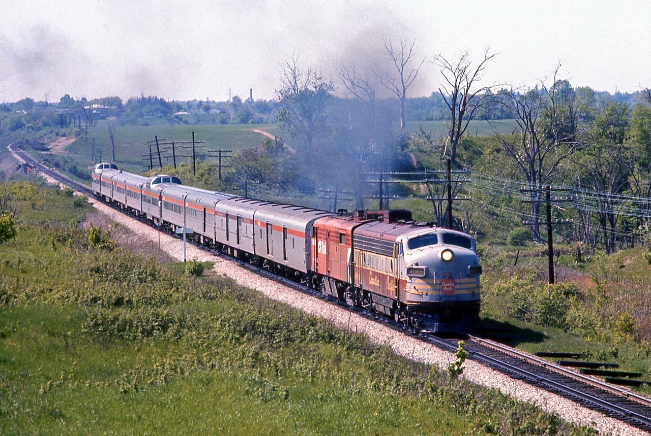 After passing through Woodbridge (no longer a scheduled stop as the station had closed a few years earlier) CP train #12, the Sudbury-Toronto section of The Canadian crosses the Humber River and heads south on the Mactier Sub, passing the white Emery mileboard sign and about to duck under the CN Halton Sub just west of Islington Avenue on the Vaughan-Toronto border.CP repainted its 1400/1900-series passenger locomotives and stainless steel Budd equipment used on the Canadian relatively quickly after the new CP Rail branding was introduced in 1968. But, dual-service (freight/passenger) locomotives often found in passenger service, such as FP7 4066 leading, continued to operate in their older colours for years until overhaul or repainting. The trailing repainted FPA2 is likely one of the dual-service 4094-4097 group that also frequented #11/12.The consist today is two older lightweight steel baggage cars (one still with the maroon stripe, both painted silver to match the newer Budd stainless steel cars), a baggage-dormitory car, coach, Skyline dome, a Manor and a Chateau sleeper, dining car, and the dome-observation "Park" car on the tail end.A wider approach shot of the same train: http://www.railpictures.ca/?attachment_id=25781