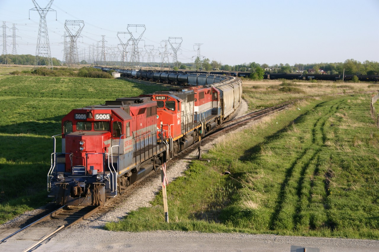 RLK 5005, RMPX 9431 and RLK 4057 quietly wait for the evening crew to take SOR 597's daily freight to Brantford and CN interchange.  This photo of SOR 597 and surrounding trackage was taken from Concession 8 (south edge of the Garnet Yard)looking southward. The still standing trackside switch cabinet in the distance (mile 4.4) marks the crossing site and diamond of the former CN Cayuga Subdivision and the Hagersville Subdivision. The connecting track still exists plus part of the Cayuga Subdivision to the west (almost to Regional Road 55. SOR continue to utilize this trackage for tank car storage.  The n/w connecting track has been disconnected at the westerly point. Fast forward to this day and same location ... now its G&W livery / colours, numerous wind turbines and drone photography.