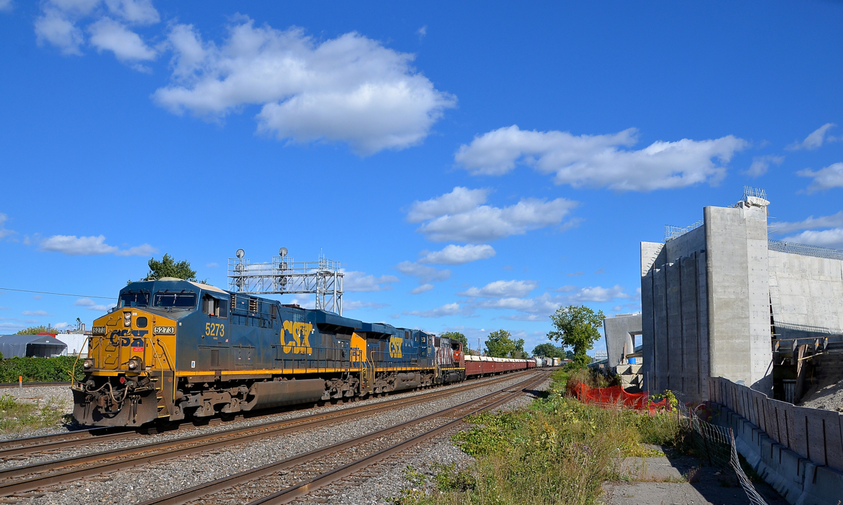 The 'overpass to nowhere' will soon go somewhere. CN 327 has a pair of CSX ES40DC's and a CN GP38-2W (CSXT 5273, CSXT 5277 & CN 4762) and 97 cars as it passes an overpass with an interesting story. Transports Québec started building an overpass which would bring highway 20 to the nearby airport about 6-7 years ago, but then realized that it had not obtained permission from CN or CP to build pillars on their right of way. Part of the overpass at right had sat unused and useless all this time, but work has finally begun anew as an agreement with the railways was reached a year ago.