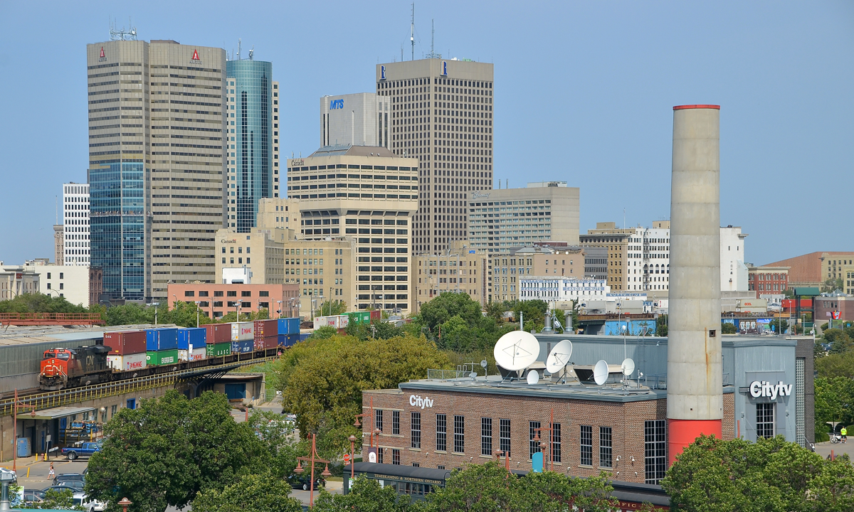 Through downtown Winnipeg. CN 2915 leads CN 101 through downtown Winnipeg. CN 2939 is mid-train and new ET44AC CN 3079 is on the tail end of this long (14,147 feet) intermodal train.