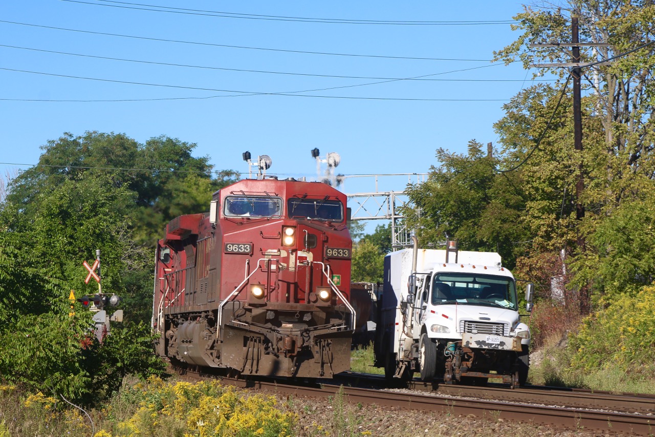 A CP high rail truck occupies the north track at Streetsville. The workers are busy maintaining the switch into the Ardent Mills facility and are briefly taken away from their work in order to inspect an eastbound train as it thunders past.