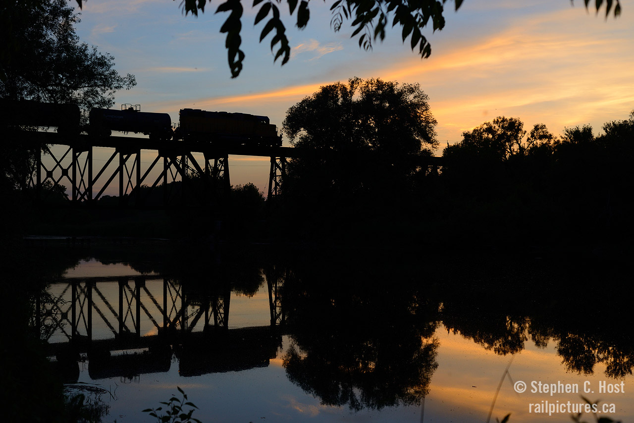 Still waters of the Conestogo river reflect a yellow and orange sunset, and a train: GEXR 584 with tank cars is northbound for Chemtura in Elmira. Mosquitos were biting every square inch of exposed skin as I took this photo, and it was more than worth it.