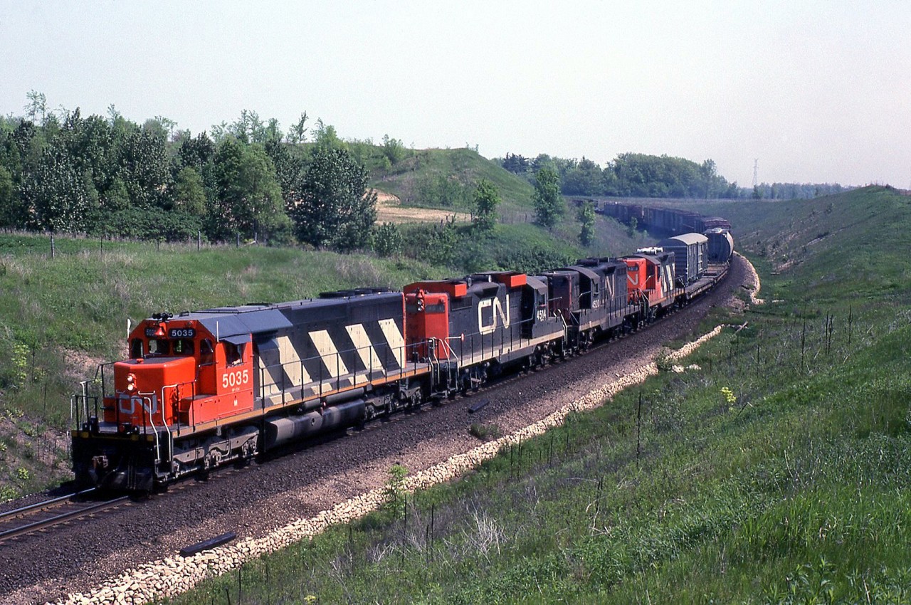 CN SD40 5035 leads GP9's 4514 (outfitted for snowplow service in southern Ontario), 4520 and 4576 on an eastbound up the Halton Sub near "Mile 30", north of Milton on June 1st 1979. The flatcar just behind the power is carrying a narrow-gauge export boxcar, possibly built by National Steel Car for Africa.