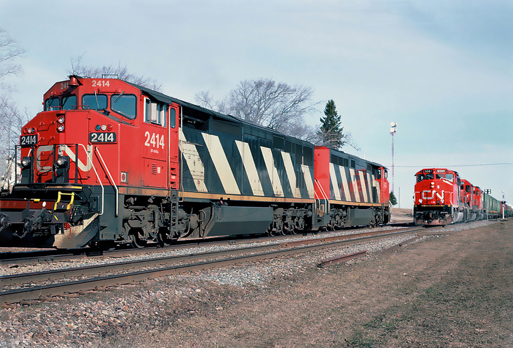One year old Canadian National GE C40-8M's number 2414 and 2420 are waiting for a meet with southbound CN 402 with in the lead GP40-2L(W) 9586 at Rogersville, New Brunswick April 20, 1991