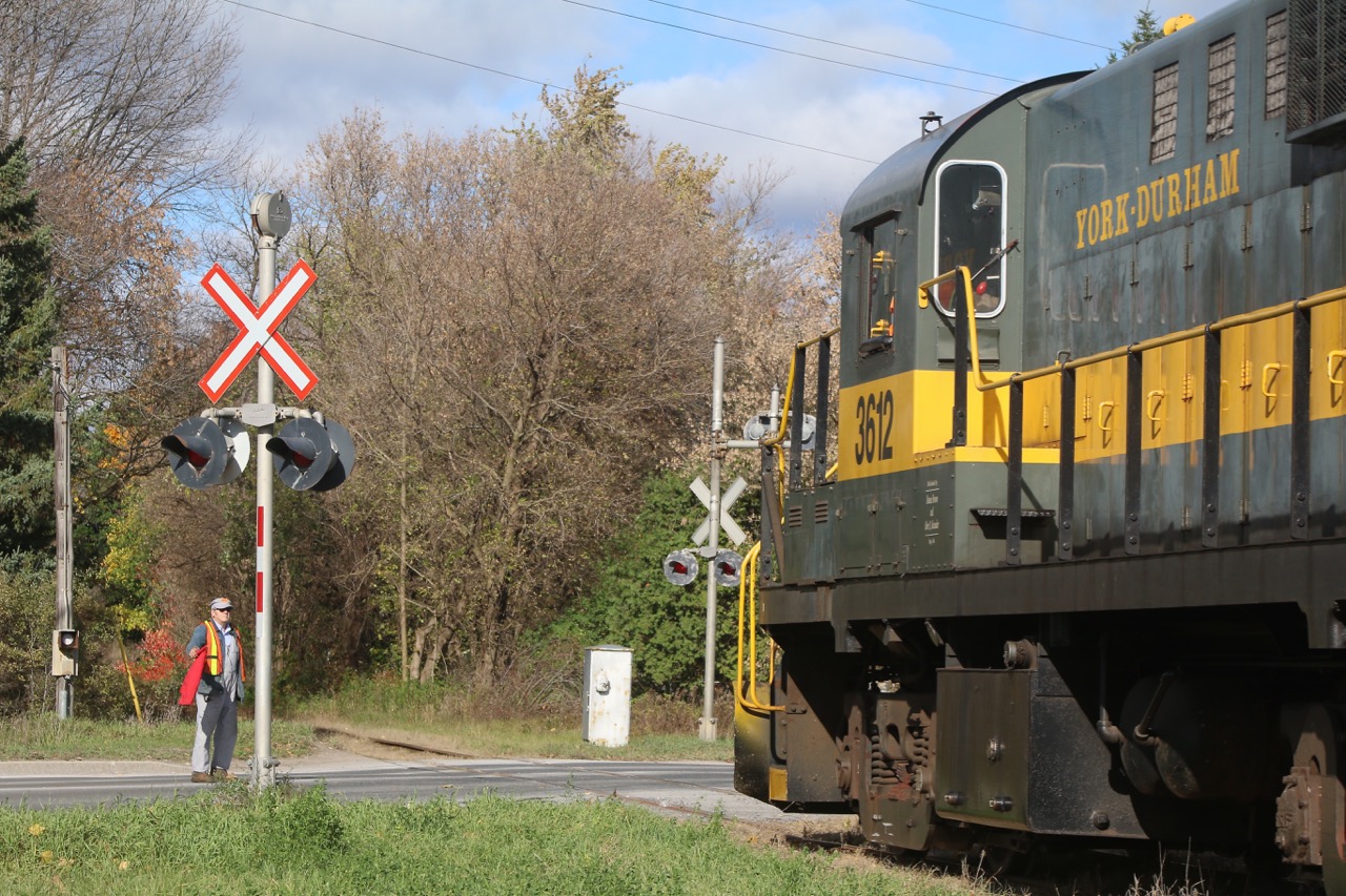York-Durham railways "Halloween train" slowly creeps towards the crossing in Goodwood, while a crew member flags the crossing. Veteran RS11 #3612 began life on the DWP before being transferred to sister road the Central Vermont. Today the Alco calls Uxbridge home along with a pair of RS-3s.