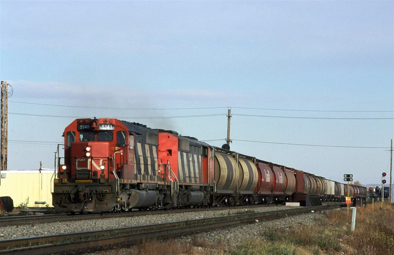 A loaded grain train arrives from Saskatoon SK on the Wainwright Sub. An eastbound grain empty may be seen at the far right, as it departs town (CN is caboose-less at this time).