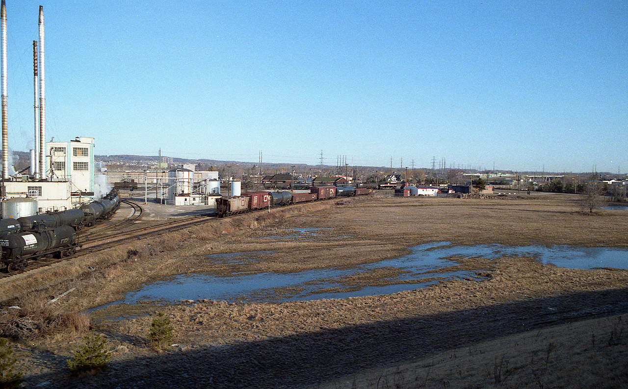 This is different. Initially I was not going to post this image, but I was convinced there may be a few of you out there in the Hamilton/Burlington area that might find this interesting. I am on the new Fairview Av overpass looking northwest. The old Burlington West CN station is in the center background, and the Hercules Chemical plant is on the left. The CN Oakville sub runs east-west in the background. "In front" of  the station is the former "yard"...there was a few industries there that were serviced by both CN and also CP, which had permission over CN into the diminutive yard. I forget whom they switched, but it probably was Hercules. You can see on the left of the photo the number of tank cars indicating they were an important customer of the railroads back then. The track that runs below me on the left is now only a stub, just enough for plant switching. The line used to run from the connection at Burlington West all the way down to Stoney Creek where it connected with the Grimsby Sub near Lake St. The line was severed around 1970 when the QEW Traffic Circle that it ran over top of, was removed. The line then ended at Lang's (Frozen) Foods. That building still stands by Confederation Park. The whole of the Beach line was removed by late 1983. In the foreground of this photo, almost dead center, stands the Mandarin Restaurant today.