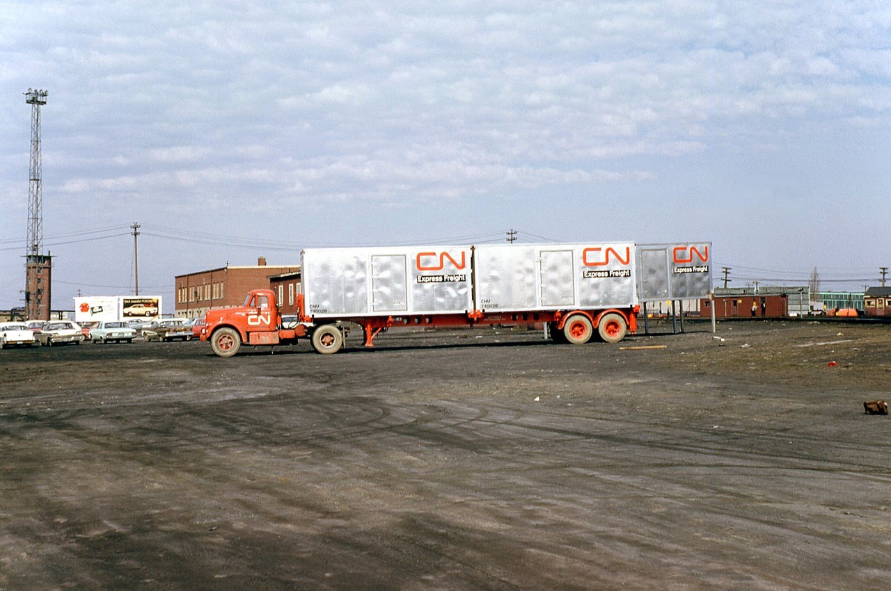 Another example of Canadian National's early intermodal container operations: a CN truck and container chassis are loaded with two smooth-side CN Express Freight containers (CNU 740028 and CNU 740026), seen in this view looking west by the yard offices at the west end of CN's Mimico Yard, by the corner of Kipling Avenue and New Toronto Street (the Mimico Yard tower in the distance is actually north of the yard and mainline tracks, with the car advertisement billboard on the west side of Kipling just before the rail underpass). Another smooth-side container on stands can be seen to the right.

Early intermodal containers loaded on flatcars in Mimico Yard: http://www.railpictures.ca/?attachment_id=26929