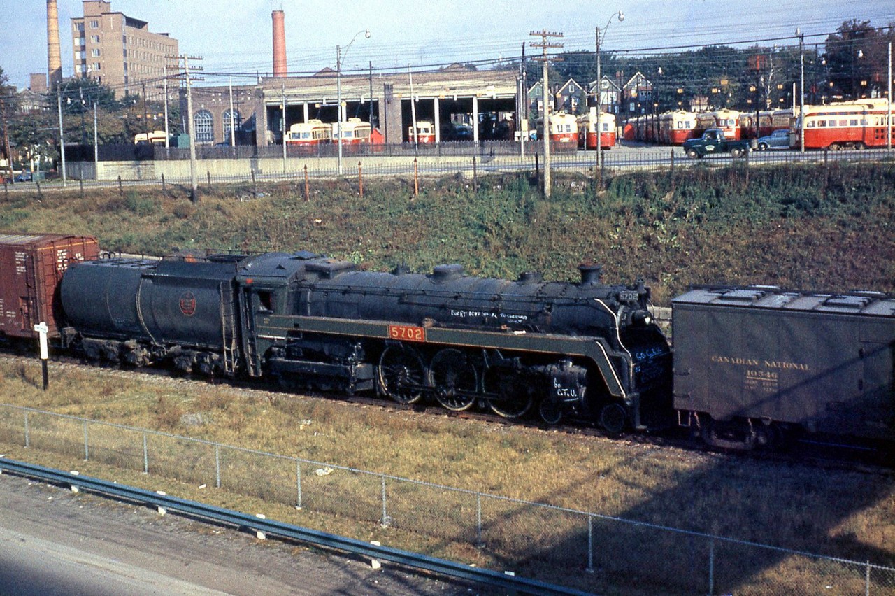 At the end of the steam era, a few examples from notable steam engine classes were either donated or set aside for preservation by Canadian National. CN 4-6-4 K5a Hudson 5702 is pictured passing though Sunnyside dead-in-tow on a freight train in October 1960, enroute to Montreal for forwarding to the Canadian Railway Museum (Exporail) in Delson for preservation. Routing or preservation instructions are written on her boiler, cylinders and front. In the background, the TTC's Roncesvalles Carbarns can be seen teaming with PCC cars, and St. Joseph's Hospital is visible on the left.