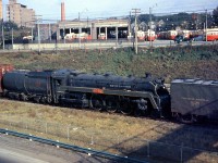 At the end of the steam era, a few examples from notable steam engine classes were either donated or set aside for preservation by Canadian National. CN 4-6-4 K5a Hudson 5702 is pictured passing though Sunnyside dead-in-tow on a freight train in October 1960, enroute to Montreal for forwarding to the Canadian Railway Museum (Exporail) in Delson for preservation. Routing or preservation instructions are written on her boiler, cylinders and front. In the background, the TTC's Roncesvalles Carbarns can be seen teaming with PCC cars, and St. Joseph's Hospital is visible on the left.