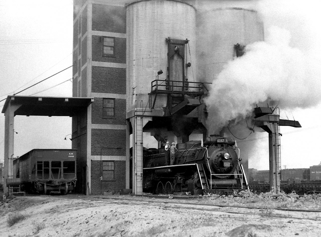 Canadian National Railway U2e Northern 6167 is pictured posed under the coal tower in Mimico Yard early in 1960. The brick and concrete coaling tower, which was located at the south end of Mimico Yard to the west of the roundhouse, was still usable despite diesel having taken over en masse.

Around 1960, the Upper Canada Railway Society approached CN about a steam locomotive for excursion service. Most of the dozen or so remaining Northerns based out of Mimico had apparently been stored serviceable, if not scrapped. 6167, still based out of Mimico, was one of a few that had been most recently retubed and had the least amount of mileage on it since, which likely played a factor in its selection over the others (operating until its "tube time" ran out in September 1964, after which its excursion duties were taken over by 6218).