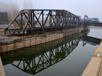  AMT 809 is arriving from the South Shore with AMT 1364 pushing it over the Lachine Canal on a foggy morning. Reflected at left is the out of use swing bridge that CN freight trains formerly used to access the Port of Montreal. 