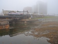 On a very foggy and windless morning, heritage unit AMTK 145 is pushing the deadheading <i>Adirondack</i> towards Montreal's Central Station. As happens every fall, the Peel Basin and connected Lachine Canal have been mosttly drained, but there is still enough water for the engine to be reflected.