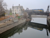 Both VIA 63 and the abandoned Wellington Tower are reflected in the still waters of the Lachine Canal on a foggy morning.
