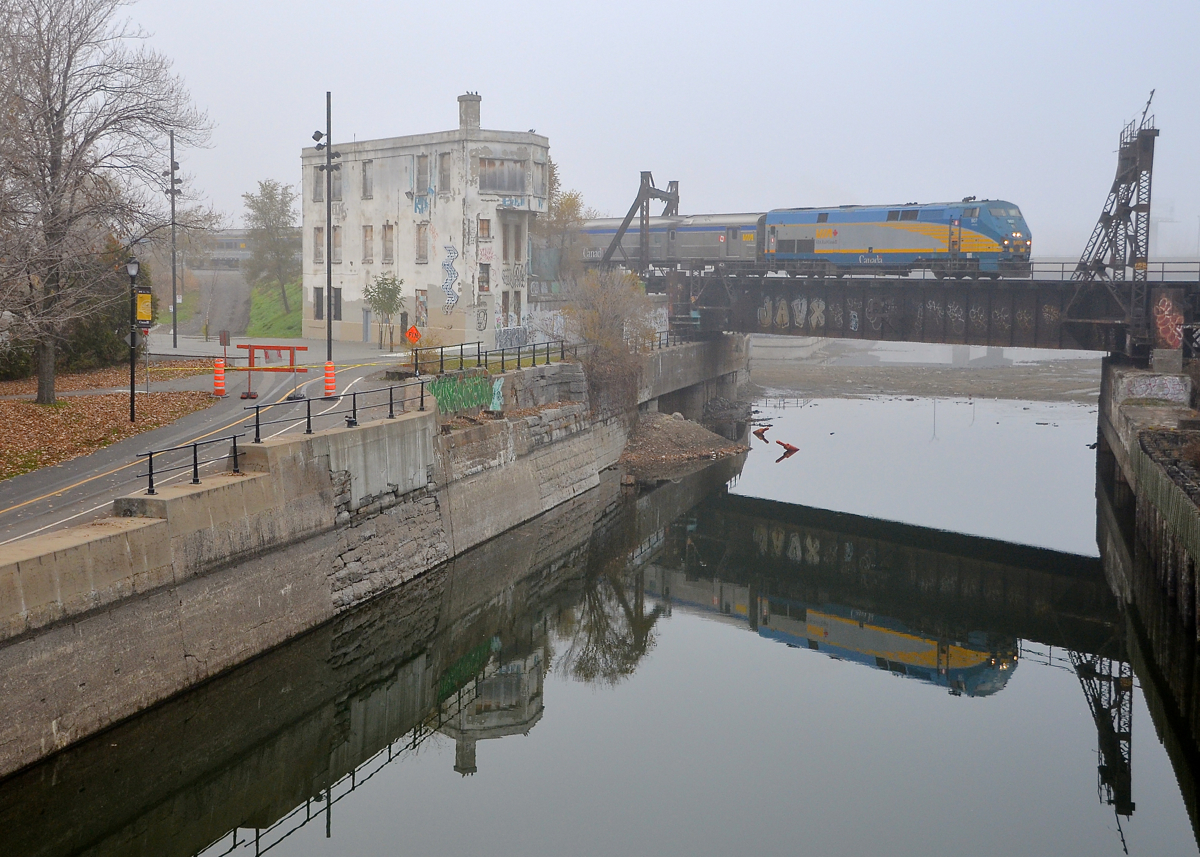 Both VIA 63 and the abandoned Wellington Tower are reflected in the still waters of the Lachine Canal on a foggy morning.