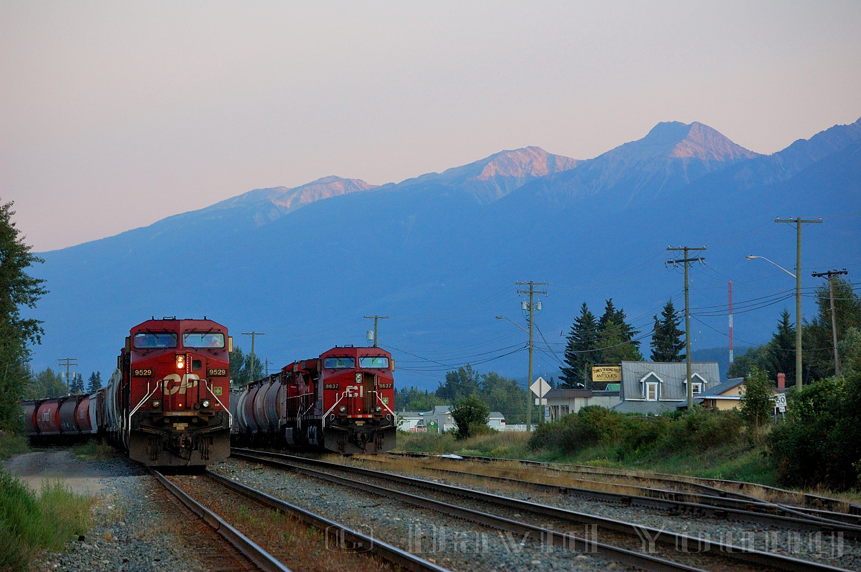 It's a warm and hazy evening in the valley, the final rays of the day glints of the snow capped peaks around Golden as CP 9529 West pauses to fuel after beating the Kicking Horse. It's next challenger: Rogers Pass. In the background on one of the yard tracks CP 8637 West sits awaiting its crew after switching downtown.