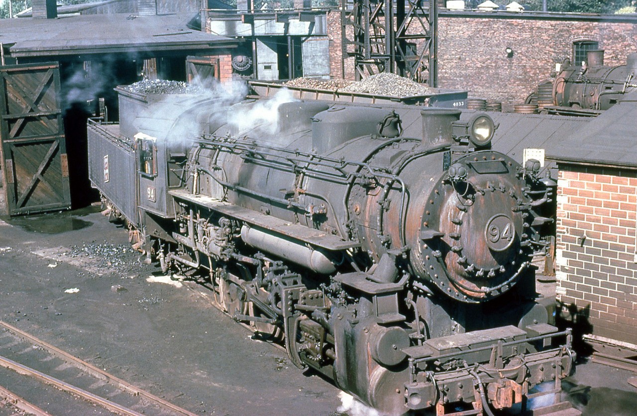 Sydney and Louisburg Railway 0-8-0 94 is seen here outside of the shop in 1961, with other S&L steamers visible outside, and tucked away in the roundhouse. 94 was built by Alco in 1944 for the Pittsburgh & Lake Erie as P&LE 8061, S&L bought her in November 1956 and renumbered her to 94 (one of 8 ex-P&LE steamers acquired by S&L around that time, numbered 88-95). S&L dieselized in the early 1960's with secondhand RS1's from SOO Line and Minneapolis & St Louis, as well as three new MLW RS23's, and 94 was eventually scrapped in November of 1961.

(Original photographer George Schaller, duplicate slide from the collection of Bill Thomson and posted on behalf of and with Mr. Schaller's full participation).