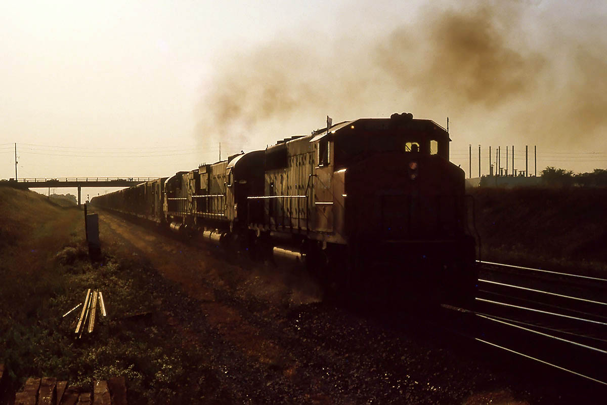 Coming out of the setting sun, with sanders on full, a GP40-2 and 2 big MLW's drag 392 out of a crew change stop with most of the train still hanging in the Humber River valley.