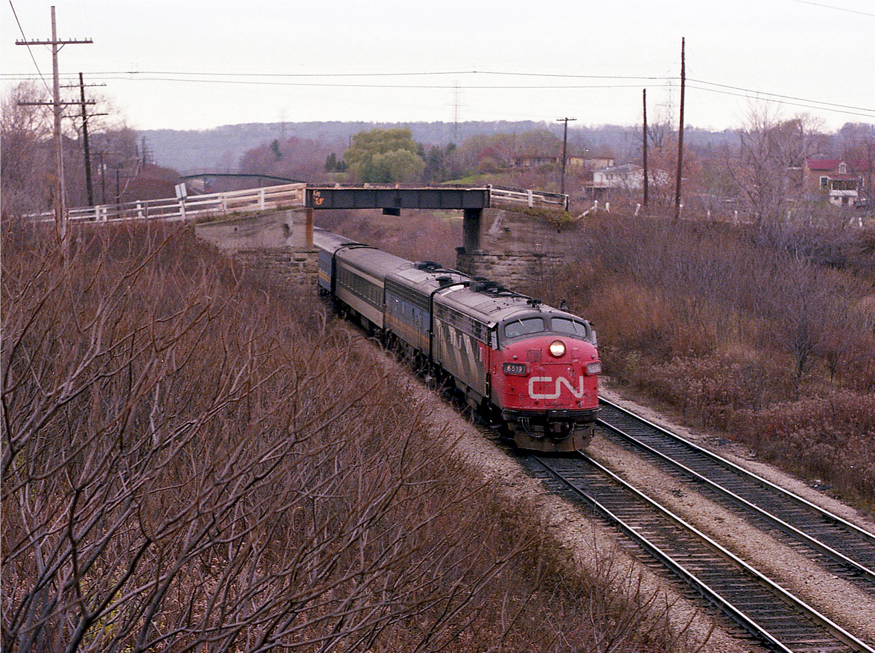If it wasn't for that walkbridge in the background of this scene, the location might be hard to identify. That little shortcut is the walkway from Homestead Av to the Bruce Trail Headquarters in the Hamilton Botanical Gardens. I am standing on the side of the CP bridge over the CN Dundas looking toward Mile 1, and morning train #84 with CN 6519 on the lead, is coming at me under dangerously decrepit old Guelph Rd bridge, which was thankfully replaced many years ago. This miserable dull day was the first day of CP detours down from Guelph Jct after the famed Mississauga Wreck of Nov 1979. I was getting restless over the lack of hopeful traffic, and went for a walk, but keeping very close tabs on the CP.:o)