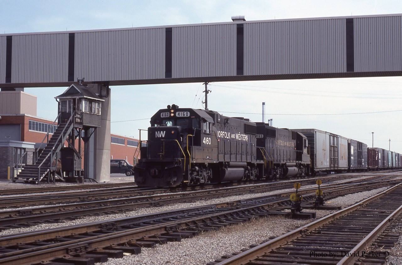 N&W ND-91 passes the Walker Road crossing gate tower (Adjacent to the Walkerville VIA station) as it arrives in Windsor, Ont on March 27th 1984 with a pair of Ex Illinois Terminal GP38-2's.  I actually worked one shift in that tower.  When CN took over the Conrail Canada Division I was working as a Car Control Clerk. When CN took over we were merged in with the CN clerks and with barely any seniority I ended up on the spareboeard. One day I get a call to work afternoon shift at the gate tower. Now the gate tower men were S&C (Signals) guys on light duties, but since they didn't have a spareboard the clerks covered any vacancies. With no training whatsoever I arrived at the tower. The guy on days said " When a train comes put the gates down. I you gotta take a leak go behind the bushes at the bottom of the stairs and if you gotta take a dump, put the gates down and go to the VIA station" and he left. There was just a phone in the tower.  Good thing I took slides to label and I called one of my railfan friends to come visit me and bring me a Harveys burger.