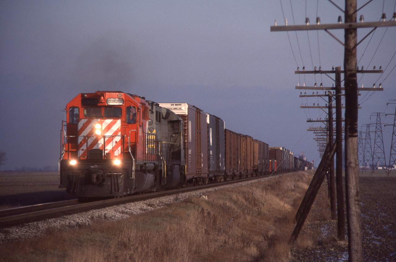 CP Extra 5550 West hustles across the flatlands of Essex County with an in-identified QNSL SD40 trailing.