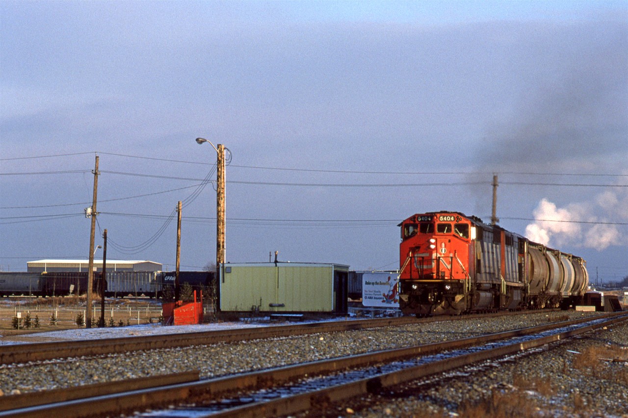 For a 500 train, 511 was a little strange. Most locals would depart and return with the same train number. 511, however, left Edmonton as 510 in the morning. It switched out the chemical plants on the Beamer Spur during the day and is returning in the late afternoon, or early evening.
Here, it is coming off the Vegreville Sub at East Junction, and joining the Wainwright Sub. The steam is from chemical plants near Clover Bar.
On the Left, near the MOW shed and dumpster, was where the mixed train to Waterways/ Fort McMurray would board passengers.