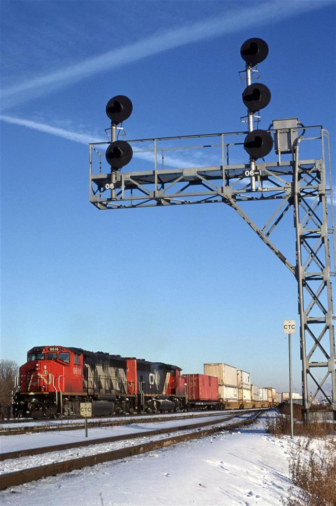 Train 117 is arriving at Calder/Walker yard in Edmonton. At the time, the intermodal yard was located between 82 and 97th Street. It has long since been moved to an area just north of Bissel Yard in the west end.
The signals control eastbound trains as they leave the yard and the yard bypass track (nearest track). Once again this has changed as there are two bypass tracks now. The sign indicates that CTC begins at this point on the Wainwright Sub. (Technically, this is not correct as the wainwright Sub used to turn SW at East Junction and go downtown. This track was controlled by the Calder/Walker Switchtender, I believe).