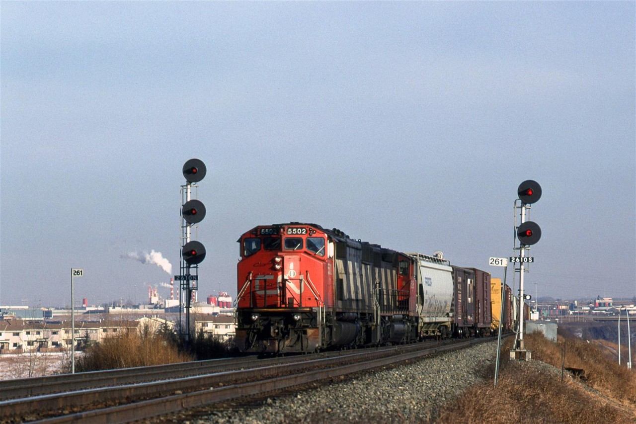 An odd looking #219 (no tank cars or auto racks) is seen at the east switch for Bailey. The rear of the trains is still on the bridge over the North Saskatchewan River 
The steam is from an Owens Corning  fiberglass manufacturing facility. The Wainwright Sub takes a big swing to the left just past the river crossing and the tracks go to the left of the Owens Corning plant.