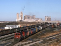 #813, a grain train for Vancouver, leaves Bissel Yard in west Edmonton. Inland Cement's plant dominates the scene.
