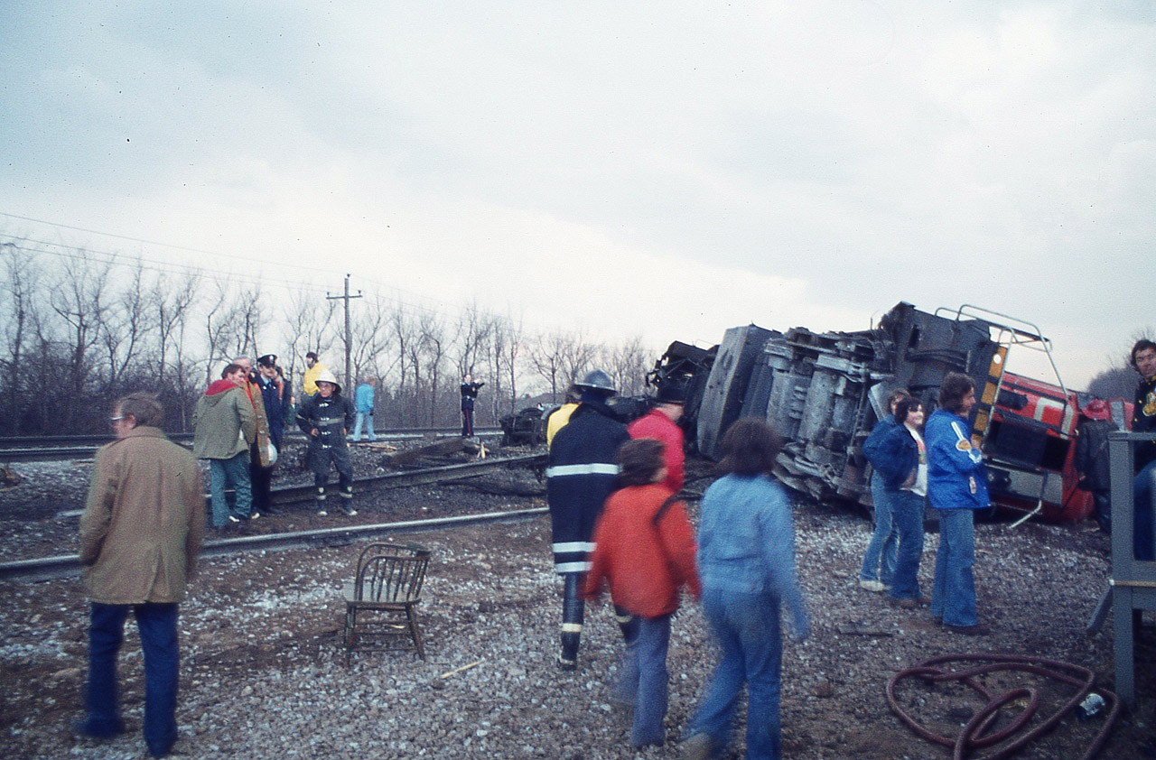 So I am standing on the Waterdown Rd bridge, quite a ways west of where I can dimly make out an approaching headlight. The sun is close to setting, I am losing light very quickly but figure before I go home I will wait this out and see what it is. Probably a passenger. As I watch the headlight coming at me, all of a sudden it appears to do a 'dipsy-doodle' and disappears. My scanner back then is still an under-dash Patrolman, fixed in the car, so I have no idea what is going on. So I go over to King Rd for a drive. There is the unit, CN 3102 laying on its' side. Passenger cars are fine, power has gone AWOL. The racket has attracted a small group of onlookers already, milling around like this was a flea market and someone was looking for perhaps a used chair. Remarkable, the lax security. Another age, another era. I wandered around for about 10 minutes, shooting pictures, most of them poor, as I had to hand-hold at 15th sec due to rapid loss of sunset light. This photo I picked up a board to use as a monopod. Not great, but it recorded the scene. No one hurt, as far as I know; and I never did find out what caused the unit to flip as it passed over King Rd grade crossing.
