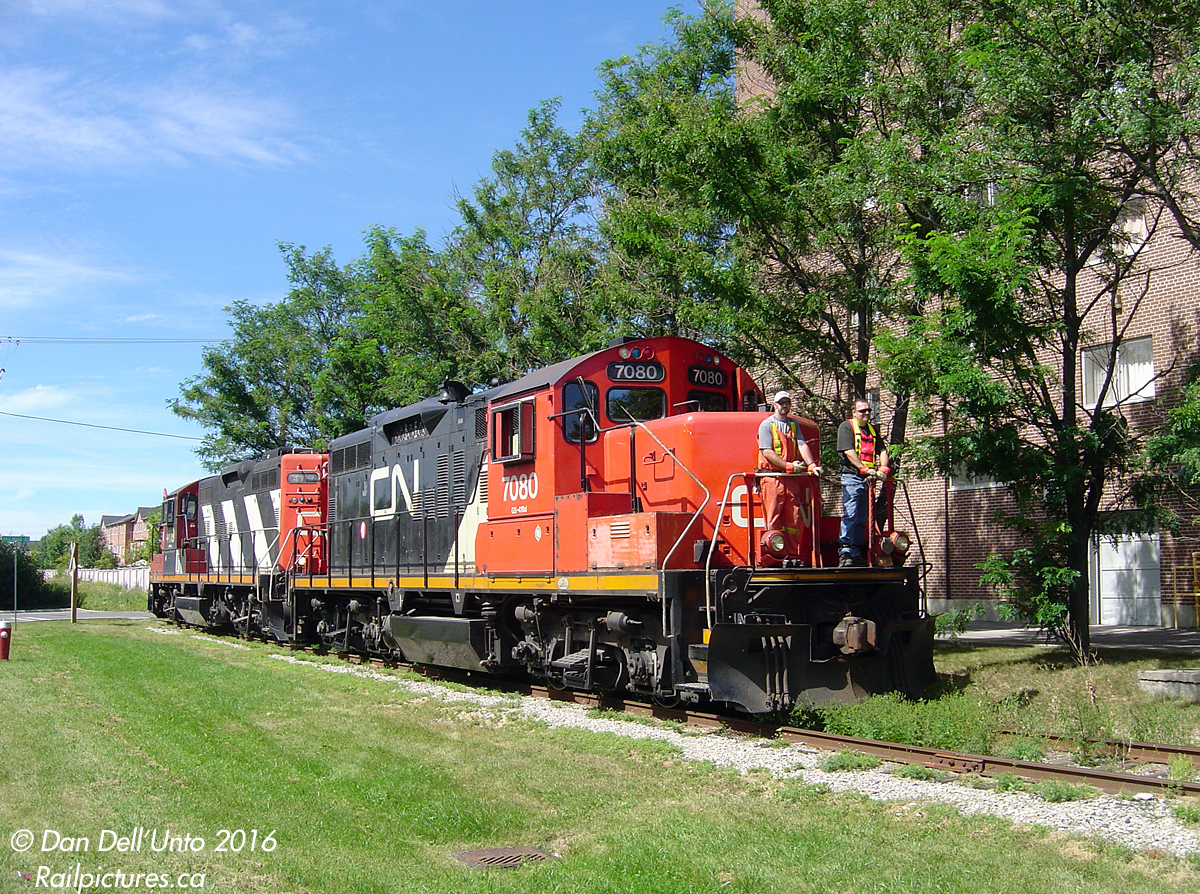 With conductor and brakeman riding the head end, CN GP9RM's 7080 and 4119 work an afternoon local (likely #559) prowling the weed-grown Dixie Cup Spur in downtown Brampton. They've just crossed Railroad Street near Haggert Avenue, and are heading south to lift a small cut of boxcars from the Georgia Pacific plant down at the corner of Queen Street and McMurchy Avenue.

This was a right time, right place "lucky shot", as I had just feasted on two slices of Mackay Pizza and made my way from the Bramalea "M-section" downtown to Brampton station by bike, to see what was out on this nice August afternoon. Seeing the tail end of a short slow westbound freight clearing the diamond and crossing over to the south track, I deciding to try my luck and headed to my favourite spot near Fletcher's Creek. I crossed the tracks here, and saw the power already bushwacking its way through the weed garden visible behind 4119. At the time there were two Brampton area locals CN ran, (559 from MacMillan Yard that worked most of the Brampton and Peel customers, and 578 from Malport that worked most of the Bramalea customers), and the furthest and only customer west of downtown and the Peel interlocking was Georgia Pacific.

The US-based Dixie Cup Company (manufacturer of plastic and paper disposable cups and utensils) chose Brampton for a new Canadian plant that opened in 1949. It was expanded over the years, and changed ownership a few times. By the 1980's it was owned by the American Can Company, and present-day it's operated by Georgia Pacific. Locals in the area will remember the large iconic Dixie Cup styled water tower at the plant built to provide backup water for the fire department (that was torn down in 1987 after underground hydro pipes had made it obsolete). The rail spur was constructed around the time the plant was built, heading south along Haggert Ave. from CN's mainline at Mile 16.1 of the Brampton Sub (today known as the Halton Sub) crossing empty meadows and fields as the area north of the plant hadn't been developed yet. At one time, there was another customer located just to the north of the plant (since redeveloped into a residential neighbourhood).

The end of the Dixie Cup Spur came when the switch off the south track was removed sometime between Spring & Fall 2008, due to 3rd track installation for expanded GO Transit service on the Georgetown (Kitchener) line. It was never put back in (G-P likely switched everything to truck), and the spur was ripped up sometime between Spring-Fall 2012.