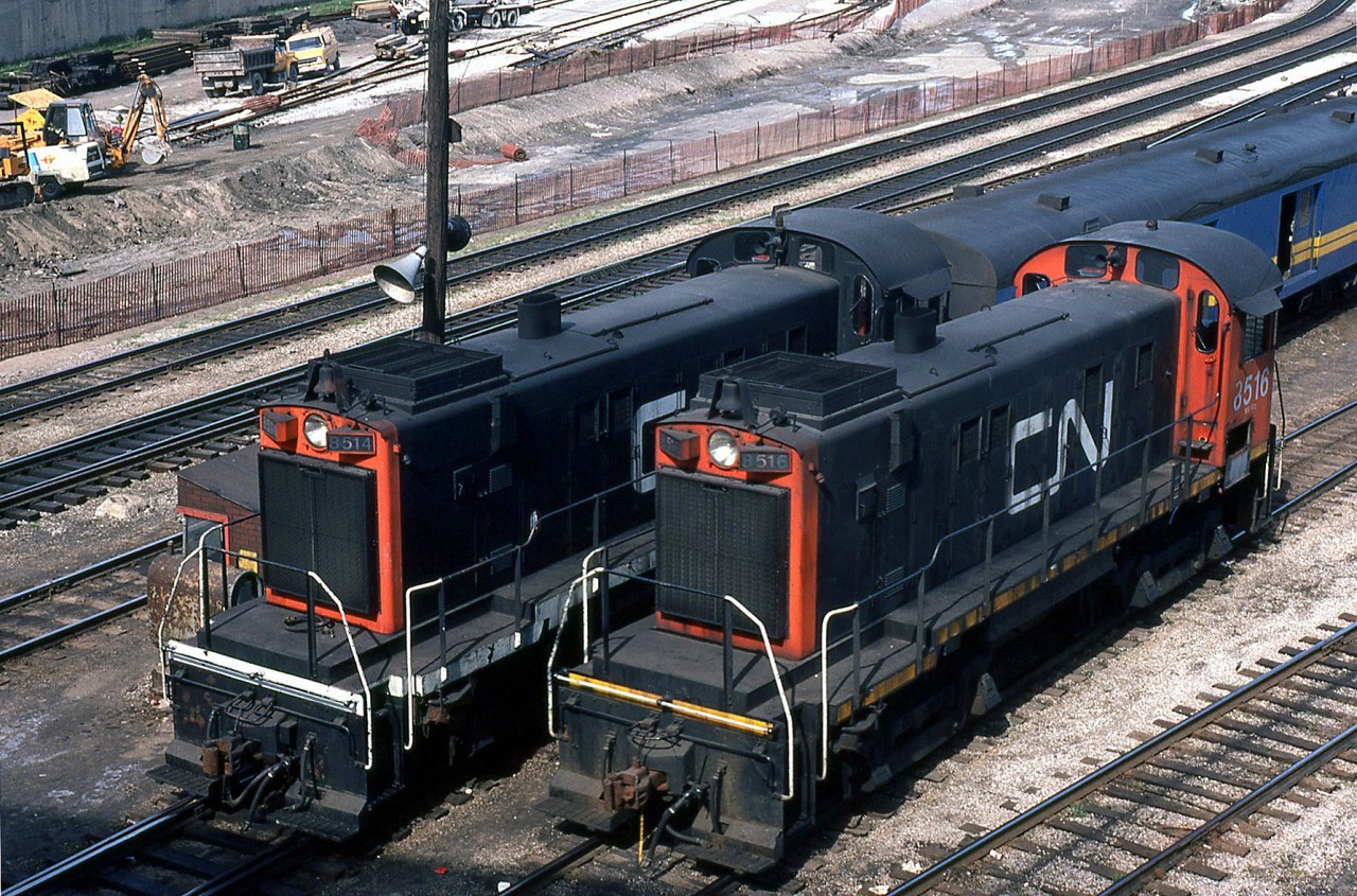CN MLW S13's 8514 and 8516 (one in the earlier noodle scheme with black cab and white frame, the older in the later scheme with red cab and yellow frame) wait at the east side of Bathurst Street Bridge, awaiting their next duties shuffling passenger cars around Spadina Coachyard, or moving train consists to/from the nearby Union Station downtown. In the background, work progresses on the future flyunder and TTR trackage around Bathurst North Yard.