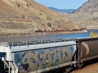 A CN Intermodal is heading west on the north bank of the Thompson River as a load of empty grain cars is heading east.