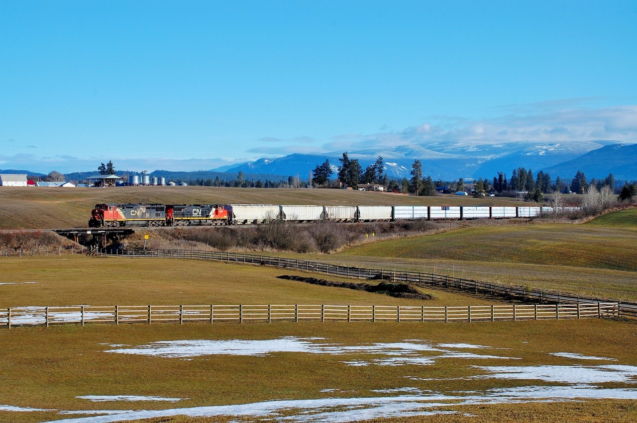 CN nos.2447&2648 are climbing out of Armstrong and are about to cross the wooden trestle over Bretts Rd. The first four cars are carrying wood pellets from the manufacturing plant located in downtown Armstrong.