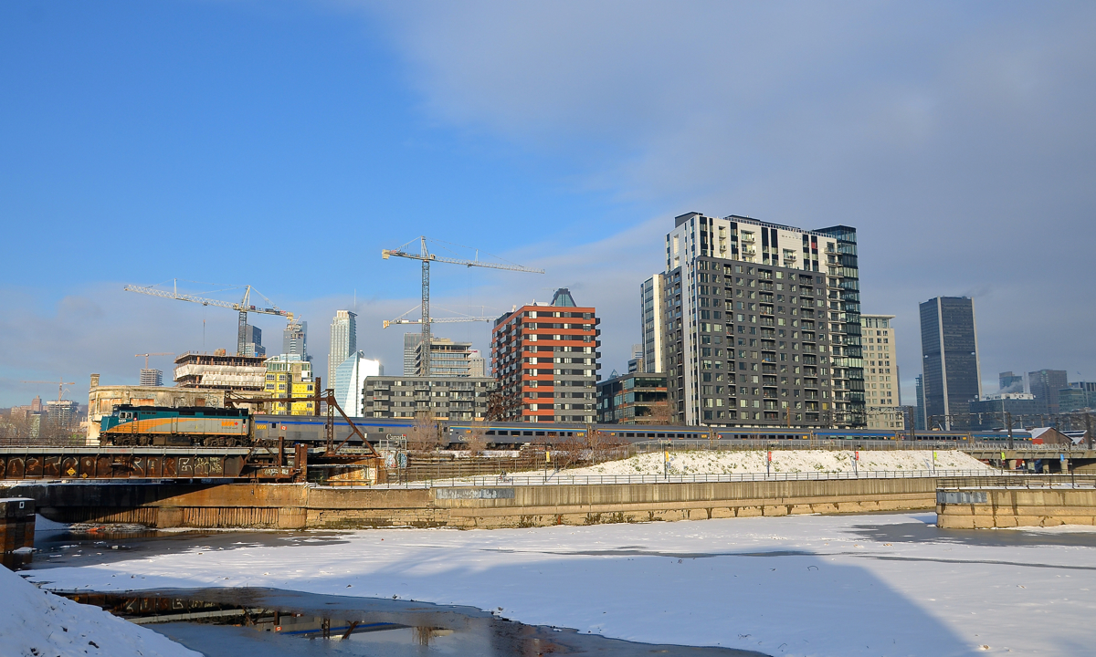 VIA 63 has VIA 6433 leading seven stainless steel cars as it passes Montreal's skyline soon after leaving Central Station.