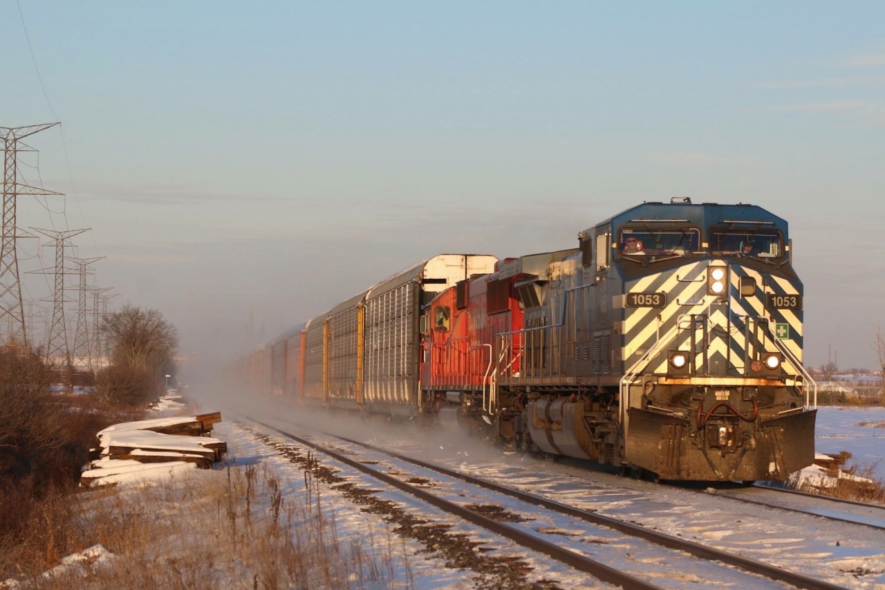 A combination of snow being swept off the ground and snow being lifted off the roofs of the auto racks by the strong wind cover the roadbed in the background as train 147 storms westward out of the dip at Hornby.