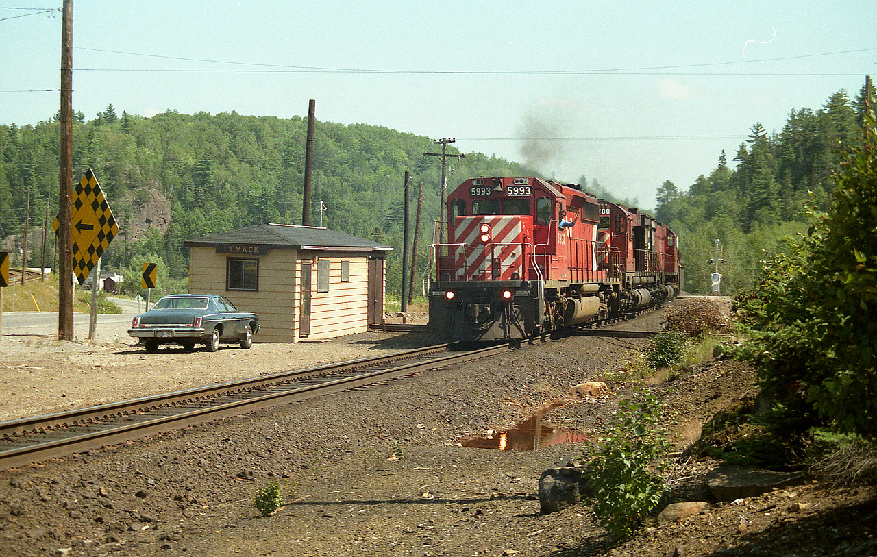 Due to the roar of some trucks on Hwy 144, I did not pick up the rumble of the train until it was almost upon me, but the conductor must have spotted me a ways off. I had seen him before, probably at Cartier station. Friendly feller. :o) His exuberance in my opinion adds a lot to the photo; CP 5993, 4700 and 5735 northbound passing Levack Station. On the extreme left you can see the INCO track leading in from the mine(s) at Onaping. Not sure what they use now, but back then I only saw GE electric 100 tonners. Behind me there is a small yard in which loads and empties are exchanged.