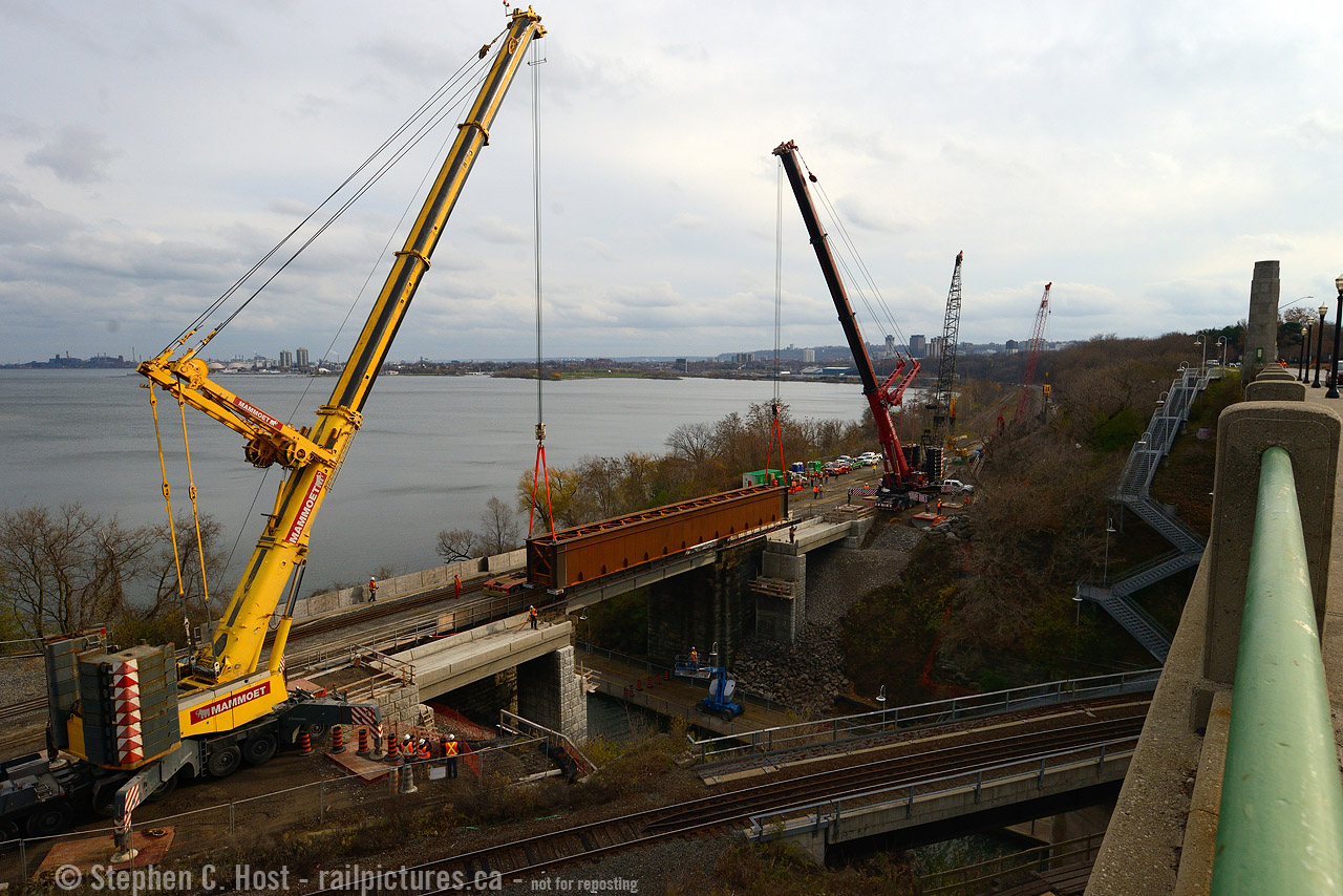 First, a history lesson The first railway bridge at this point was opened across the Desjardins Canal in 1855, as a swing bridge (!) but Canada's third worst Railway disaster occurred here in 1857, a Great Western Railway train crashed through the bridge into the icy Canal. It took two years to rebuild the bridge anew and the abutments are all that survives - the bridge having been modernised a couple times since. The TH&B/CPR added a second span in 1897 to cross over to the other side of Burlington Heights to connect the TH&B to Toronto. A third span was  added in 1993 (Reg Button photo) for the GO Hunter St expansion. 
In this photo cranes from Mammoet are lifting the fourth Railway span - a new 104 foot, 206,000 lb structure into place, with welders from the Ironworkers Local 736 ready to start work as soon as the bridge rests on its new footings. This bridge span was constructed in North Bay by Central Welding and Iron Works and the project is funded by Metrolinx as part of the James St North and Niagara Region GO improvements.
How long did it take to lift the bridge off that waiting truck and place it on footings? 10 minutes. That's it. I was simply in the right place at the right time - having gone down for the Xmas train scheduled to depart at 1400. 
Note: Research to find information used in this caption was performed by the Author. Please credit appropriately if this information is used elsewhere as considerable effort went into this caption. Thank you.